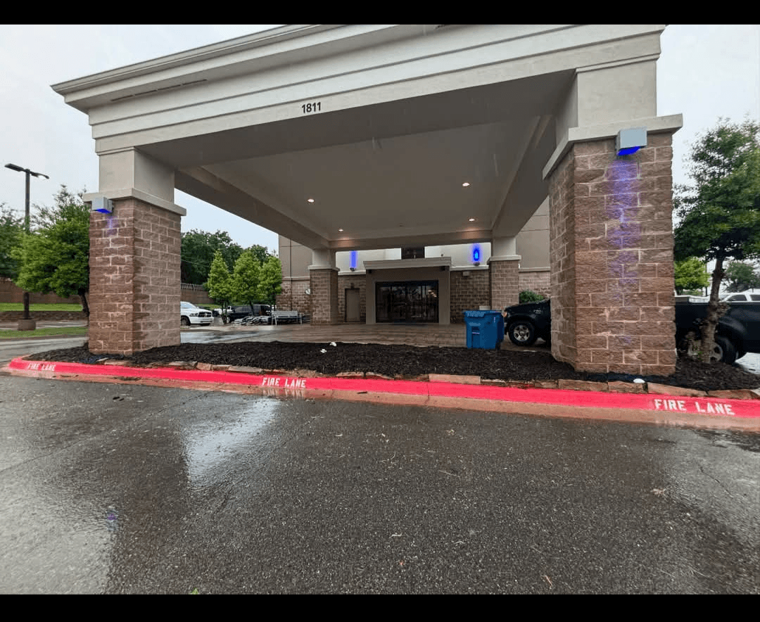 Building entrance with stone pillars, white overhang, and a red fire lane curb.
